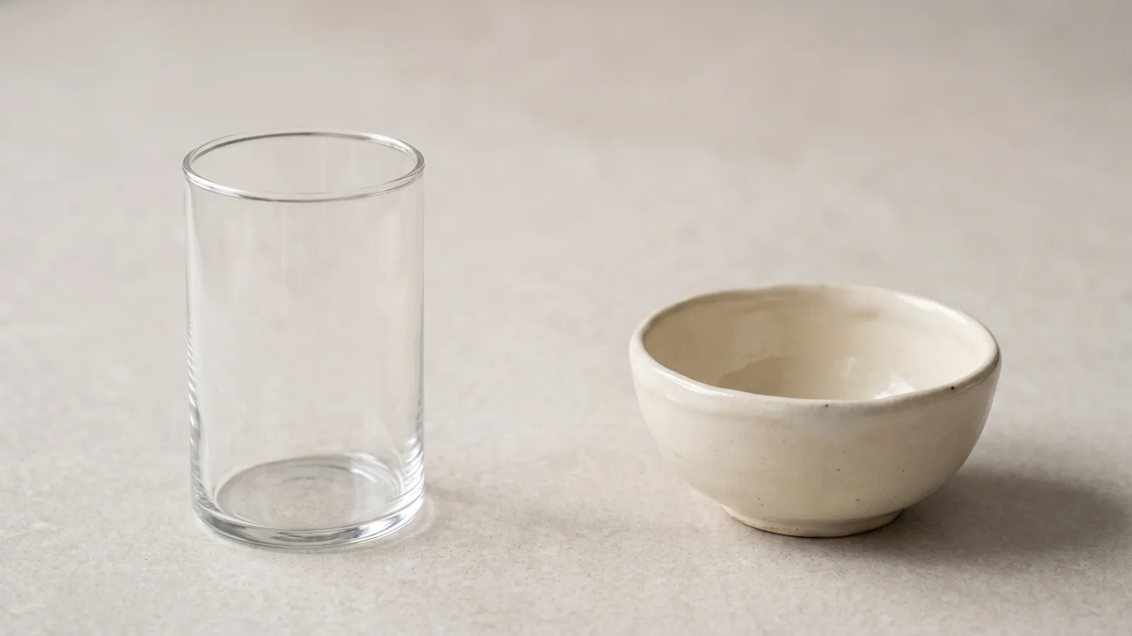 Blankt glas og håndlavet mat keramikskål side om side på lys sten
