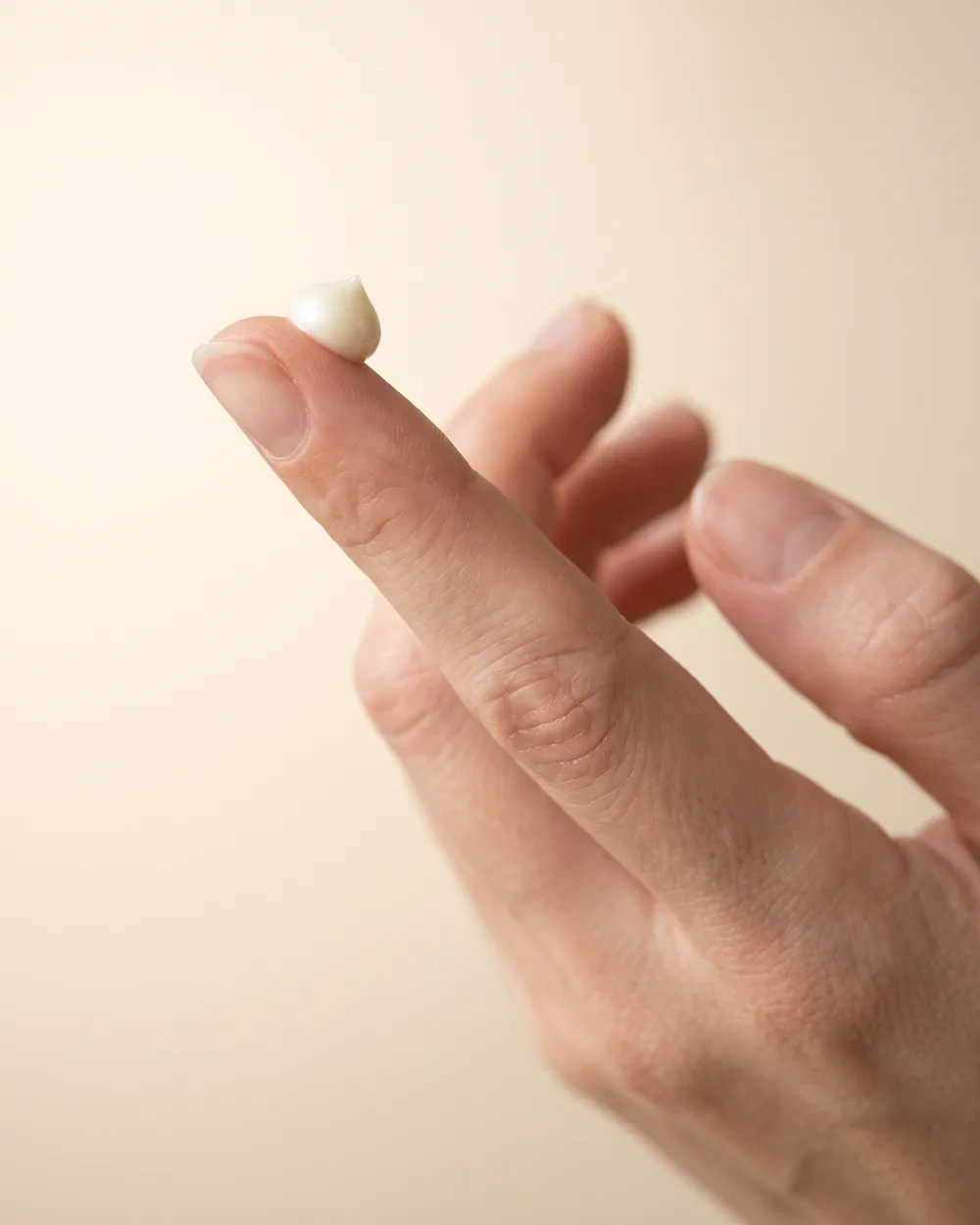 Kvindes ringfinger med en lille perle creme på fingerspidsen